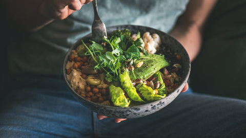 Woman in t-shirt and jeans eating vegan Buddha bowl with hummus, vegetable, salad, beans, couscous and avocado. Should I take fiber before or after meal