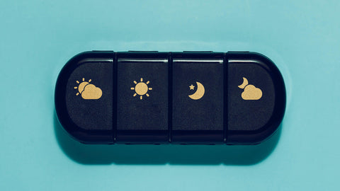 A black pill case with gold icons indicating compartments for night and day supplements for travel. A way to travel with supplements.