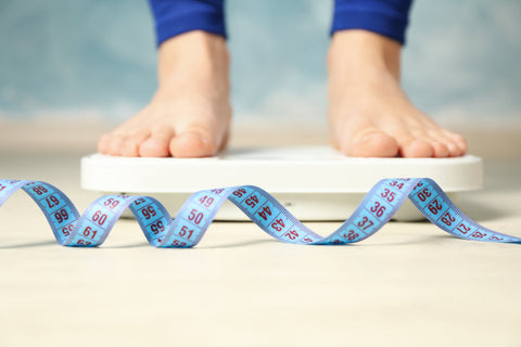 Lemon balm and weight loss, potential benefits, risks. A woman stands on a weighing scale with a measuring tape in front