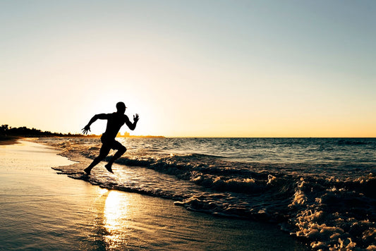 Why You Get Sore Joints from Running? Silhouette of man sprinting along ocean shore at sunset.