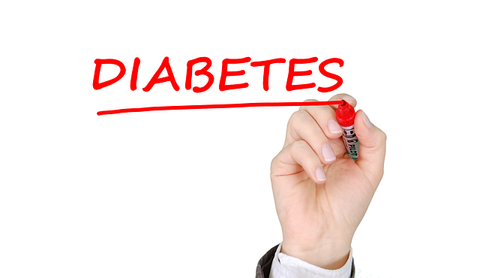 Hand writing the word diabetes using a marker that is red.