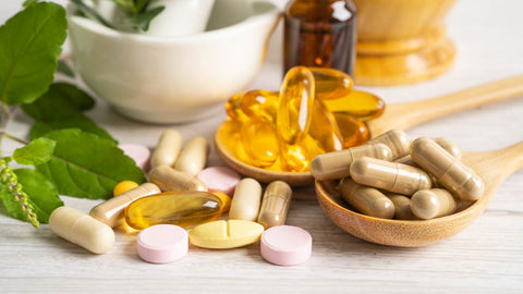 Wooden spoons with holding dietary supplements including omega 3 capsules, vitamin d, vitamin e, b vitamins, and a daily multivitamin.