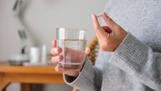 A woman is holding a white capsule and glass of water wondering about the best time to take selenium.