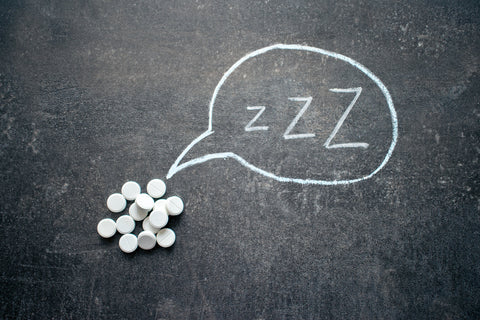 Best Vitamins for Insomnia and Sleep Deprivation. A pile of vitamins next to a chalk board with the letters Zzz on it