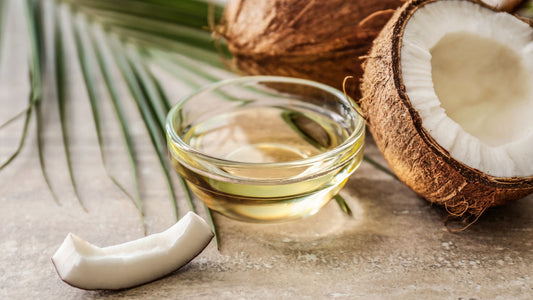 Can I Take MCT Oil on an Empty Stomach? An image of a palm leaf. Slice of fresh coconut and a coconut halved. A glass dish of MCT oil sits in the middle.