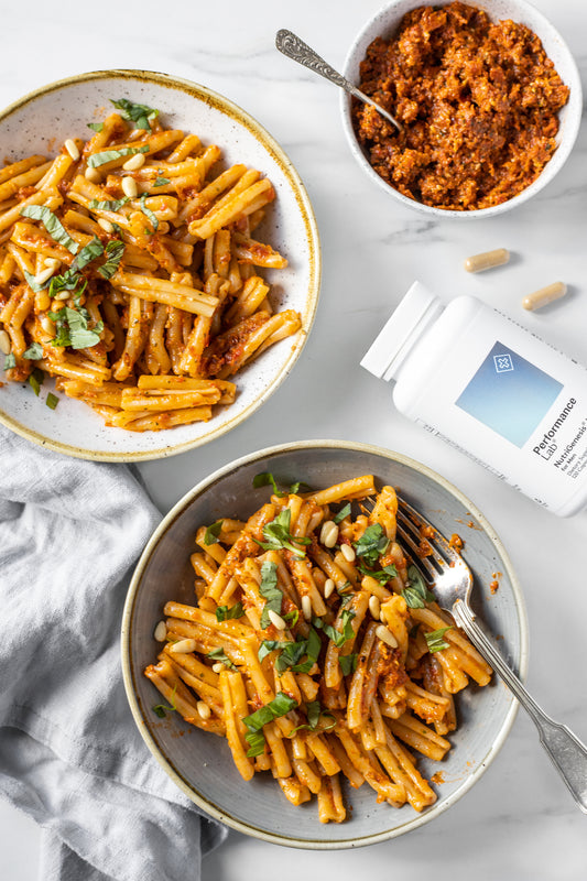Two bowls of pasta with tomato pesto and Performance Lab NutriGenesis Multi for Men on the side