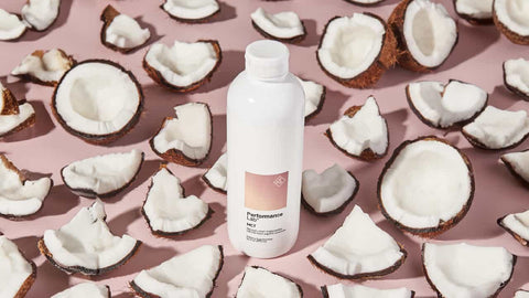 Ultimate Guide to MCT Oil Supplements. White bottle surrounded by broken pieces of coconut with white flesh exposed.