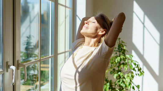 Woman indoors basking in the sun coming in through the window. Setting up the question, "Can you get vitamin d through a window?