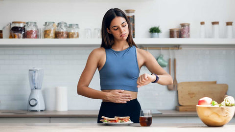 Dark haired woman in running gear looking at her watch wondering 'how long to wait after eating to run'
