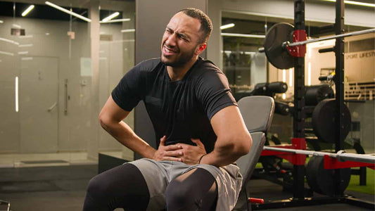 Man in gym gear holding his stomach after taking a creatine supplement. Asks the question, does creatine make you bloated