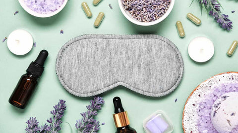 Sleep mask, lavender sprigs, essential oils, ear plugs, natural sleep aids and natural remedies shown on a green background.