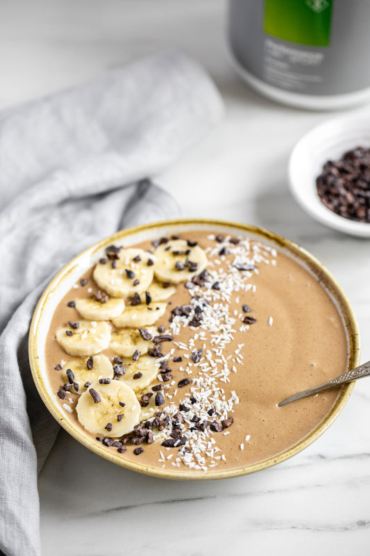 chocolate smoothie bowl with bananas and protein jar in background.
