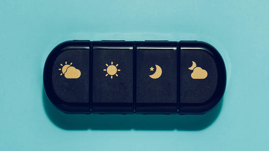 A black pill case with gold icons indicating compartments for night and day supplements for travel. A way to travel with supplements.