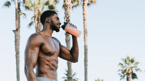 Taking Pre-Workout on an Empty Stomach: Good or Bad? A young athletic man is drinking pre-workout before exercising on the beach. 