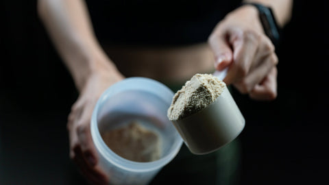 Close up of a person adding another scoop to their pre-workout shake. Conveying the point that taking too much pre workout isn’t a good thing and there are reasons to limit your dose.
