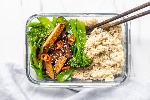 Teriyaki vegetables with broccoli and tempeh and brown rice in glass jar and chopsticks