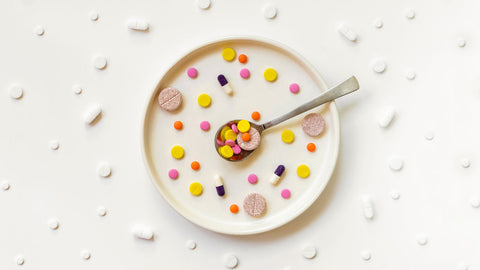 Empty plate against a light background with vitamin supplements scattered across it. Posing the question Is Taking Vitamin D On Empty Stomach A Good Idea?