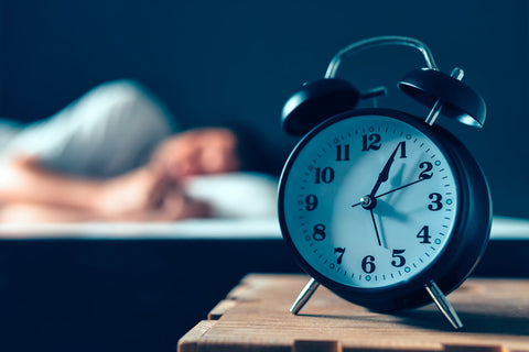 Vitamins for sleep and anxiety. A man sleeps, an alarm clock in focus in front of him