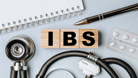 Best Supplements for IBS. Against a blue/grey background, a stethoscope, notebook, pills, a pen and wooden blocks with the text IBS. Irritable Bowel Syndrome. 