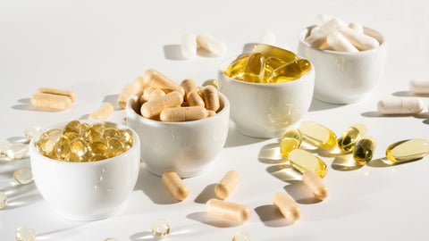 Which Is Better - Quercetin or CoQ10? A selection of softgels and capsules in small white ceramic containers and scattered on a white tabletop.