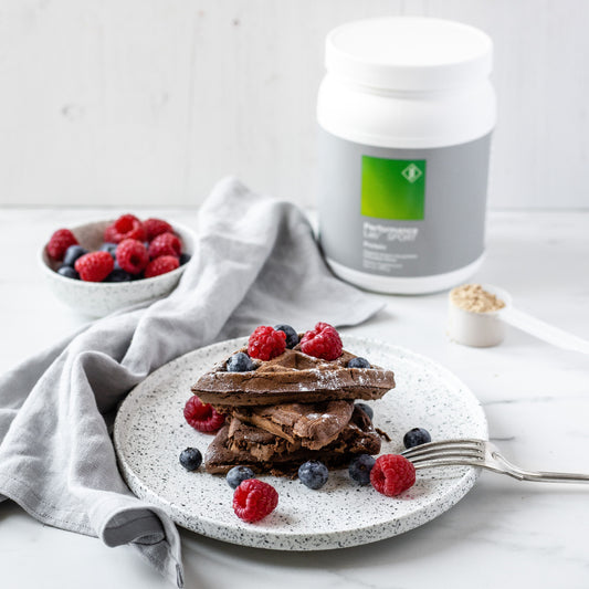 Protein chocolate waffles on plate with raspberries and blueberries and protein jar in background