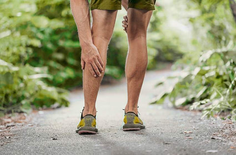 Can't Walk After Leg Day? Try These 13 Simple Tips for Optimal Recovery. A man in sports shoes on an asphalt path in nature holding his calf muscle in pain.