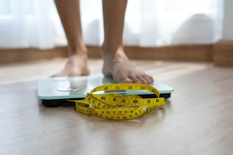 How To Know Your Metabolic Type: Feet of man on scale with measuring tape in front for body composition check
