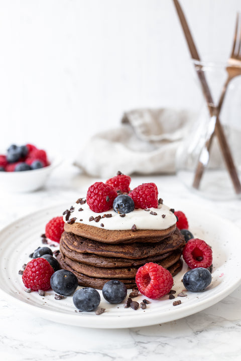 Plate with a stack of cacao protein pancakes and yogurt and berry toppings