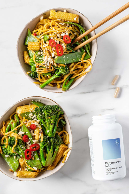 Two bowls with vegetable stir fry and multivitamin on the side with two capsules