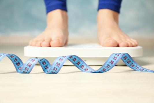  Lemon balm and weight loss, potential benefits, risks. A woman stands on a weighing scale with a measuring tape in front 