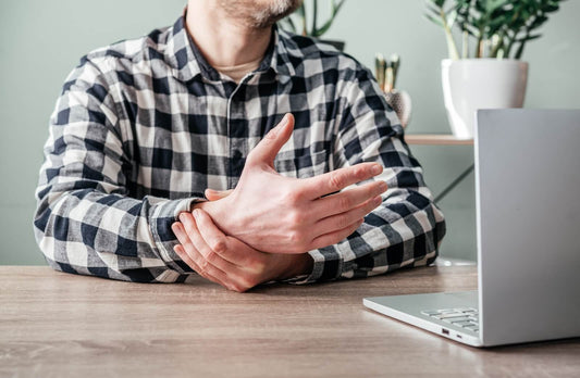 Man experiencing wrist pain while working on a laptop, showing joint strain.