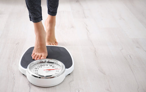 Does tart cherry extract help with weight loss? A woman stands on weighing scales placed on a light wooden floor 